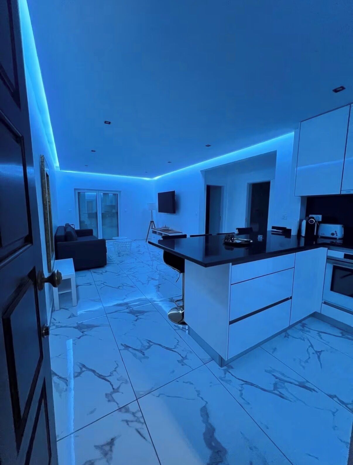 Eine moderne Küche mit Marmorboden, weißen Schränken und blauer LED-Beleuchtung.