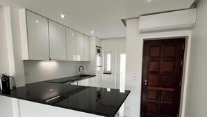 A modern kitchen with a central island, white cabinetry, and a marble floor. - Quinta do Torrejão 800m plaga Armação de pêra (Porches)