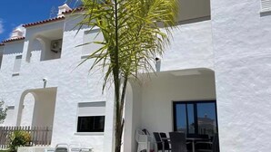 A white building with a tiled roof, a palm tree in the foreground, and outdoor seating area with chairs and tables. - Quinta do Torrejão 800m plaga Armação de pêra (Porches)