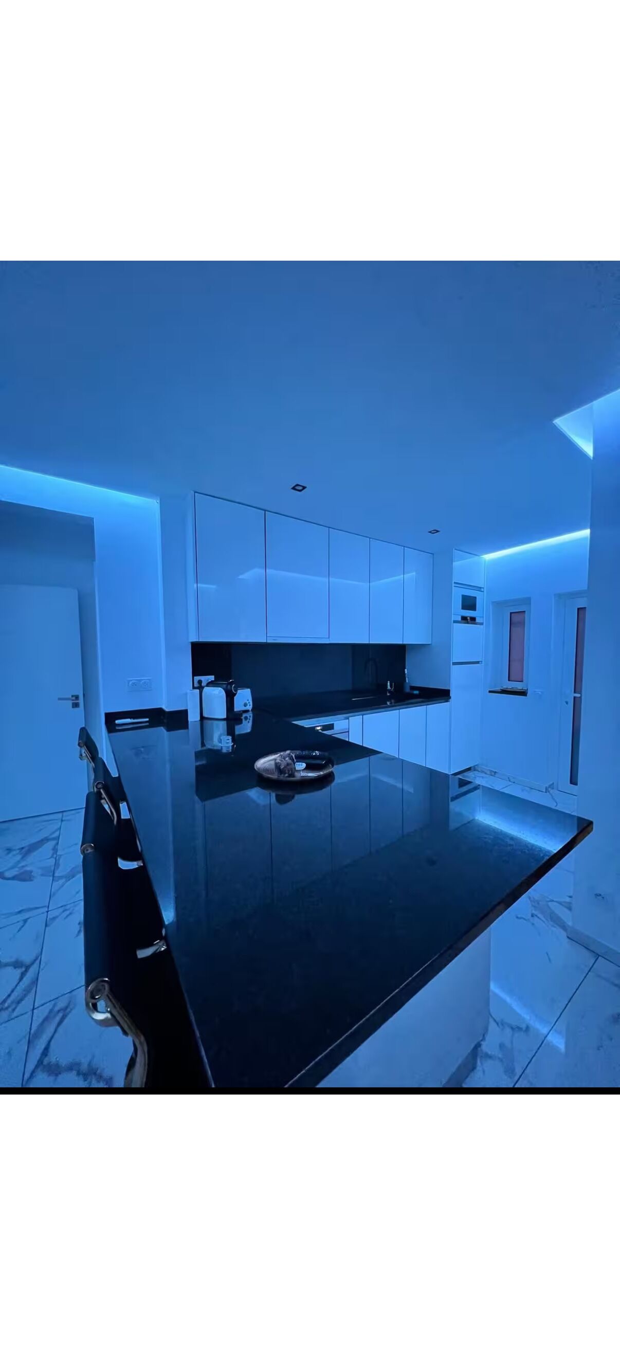 Une cuisine moderne avec un plan de travail noir, des armoires blanches et un éclairage d’ambiance bleu.