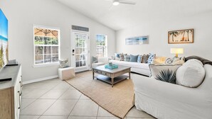 A spacious living room with a white sofa, a coffee table, and a large window with blinds. - Destin/Miramar Beach Escape, Family-Friendly + Private Beach Access (Destin)