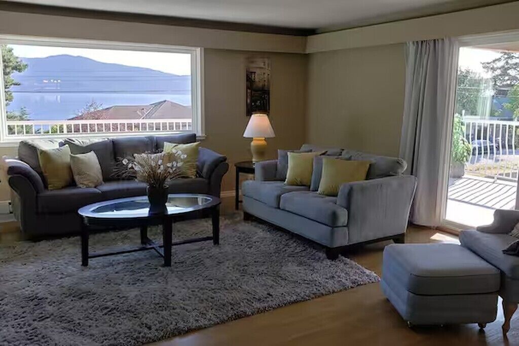 Un salon avec un canapé, une table basse et une lampe. On aperçoit un balcon et un immeuble en arrière-plan.