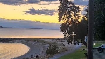 En strand med en buet kystlinje, et par personer der går, og en bygning med en veranda i forgrunden.