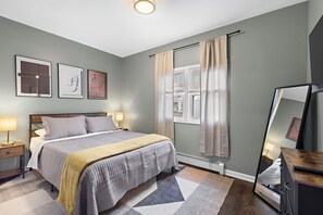 A bedroom with a bed, bedside tables, a mirror, and artwork on the wall. - Modern 3BR: 15 minutes from World Cup, Spacious, Parking + 30 minutes from NYC (East Orange)