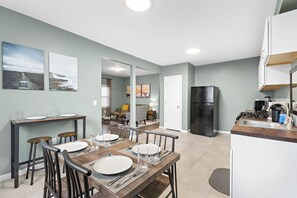 A modern kitchen with a black refrigerator, white cabinets, and a wooden dining table set for four. - Modern 3BR: 15 minutes from World Cup, Spacious, Parking + 30 minutes from NYC (East Orange)