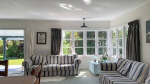 A cozy living room with striped sofas, a wooden table, and a glass cabinet. - Orange Grove Homestead - Spacious Garden Holiday Home (Kerikeri)