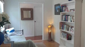 A cozy room with a bed, a bookshelf, a lamp, and a window with curtains. - Orange Grove Homestead - Spacious Garden Holiday Home (Kerikeri)