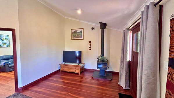 A living room with a wooden floor, a flat-screen TV on a wooden stand, a fireplace, and a door with curtains.
