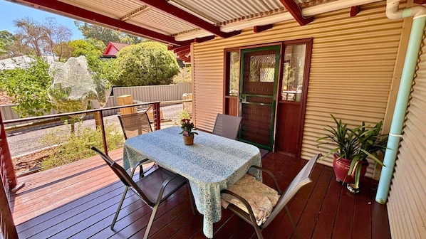 A covered outdoor patio with a table and chairs, a potted plant, and a view of the surrounding area.