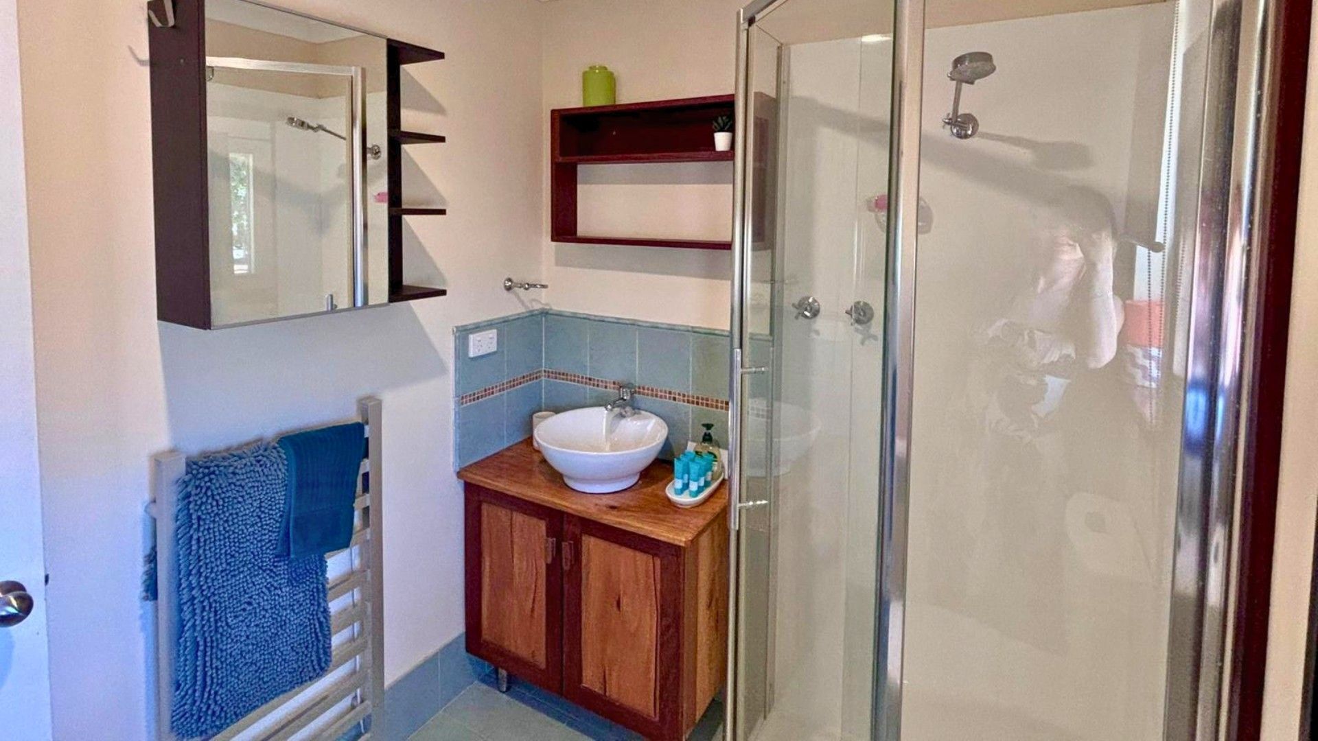 A bathroom with a glass shower enclosure, a wooden vanity with a white sink, and a blue towel hanging on a rack.