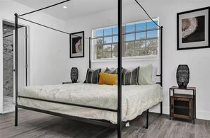 Un dormitorio moderno con cama con dosel, una ventana con persianas y una obra de arte enmarcada en la pared.