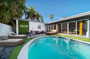 Een modern buitenzwembad met een lounge, een Dior bord en een glazen patio.