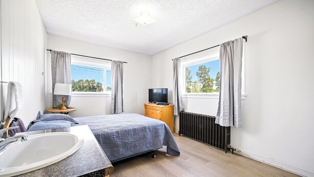 A bedroom with two beds, a TV, a radiator, and a window with curtains.