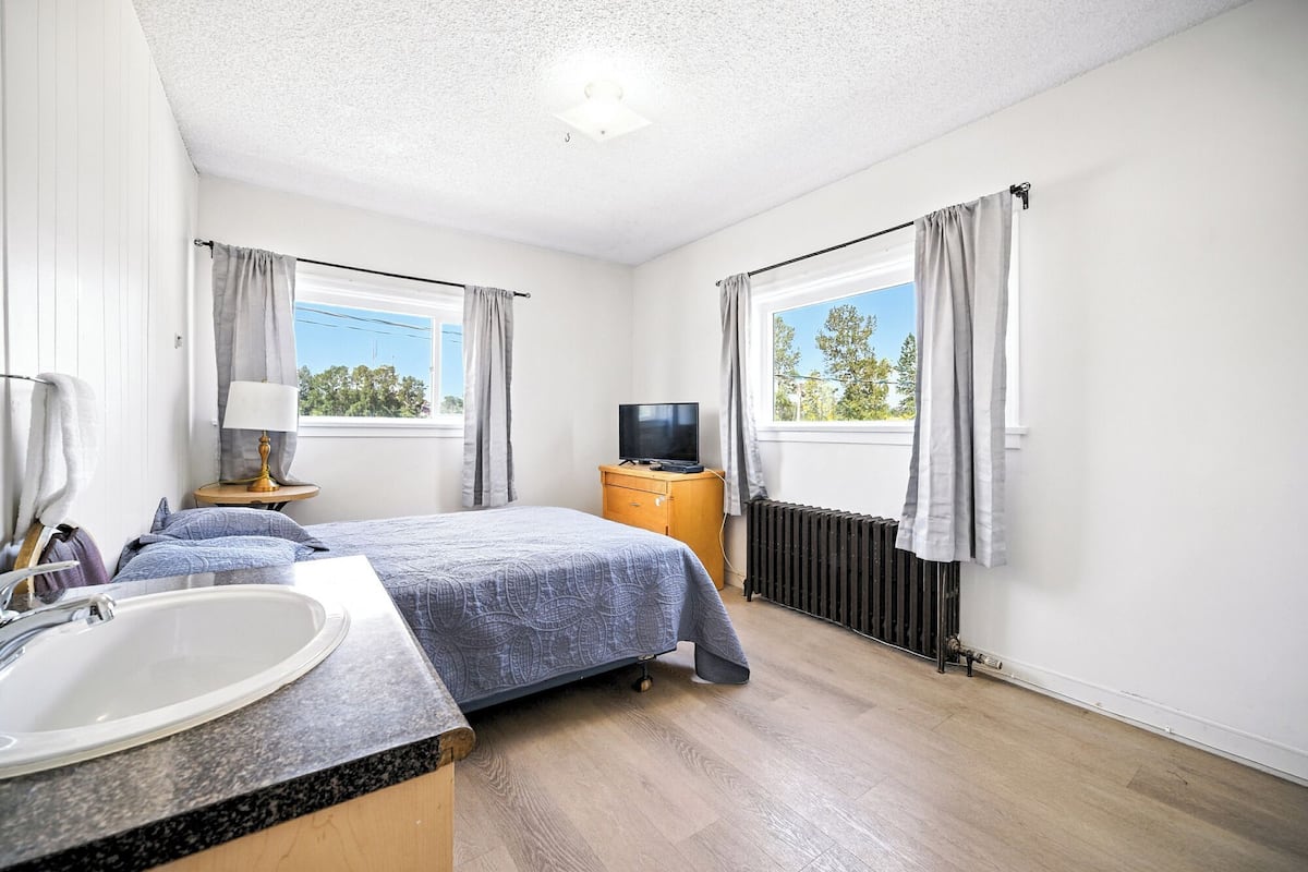 Un dormitorio con dos camas, televisor, radiador y ventana con cortinas.