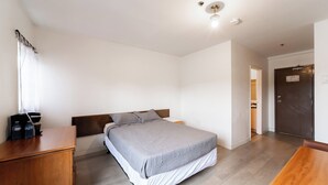 A bedroom with a bed, wooden dresser, and a door leading to a bathroom.