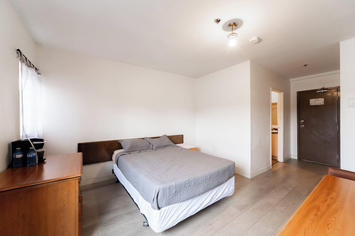 Un dormitorio con cama, cómoda de madera y puerta que da a un baño.