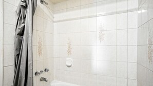 A bathroom with white tiled walls, a bathtub, and a shower curtain.