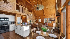 A spacious wooden cabin with a kitchen, dining area, and a staircase leading to a loft. - Smoky Mountain Views • Hot Tub • Fireplace • Cozy Cabin (Sevierville)