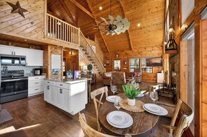 A spacious wooden cabin with a kitchen, dining area, and a staircase leading to a loft. - Smoky Mountain Views • Hot Tub • Fireplace • Cozy Cabin (Sevierville)