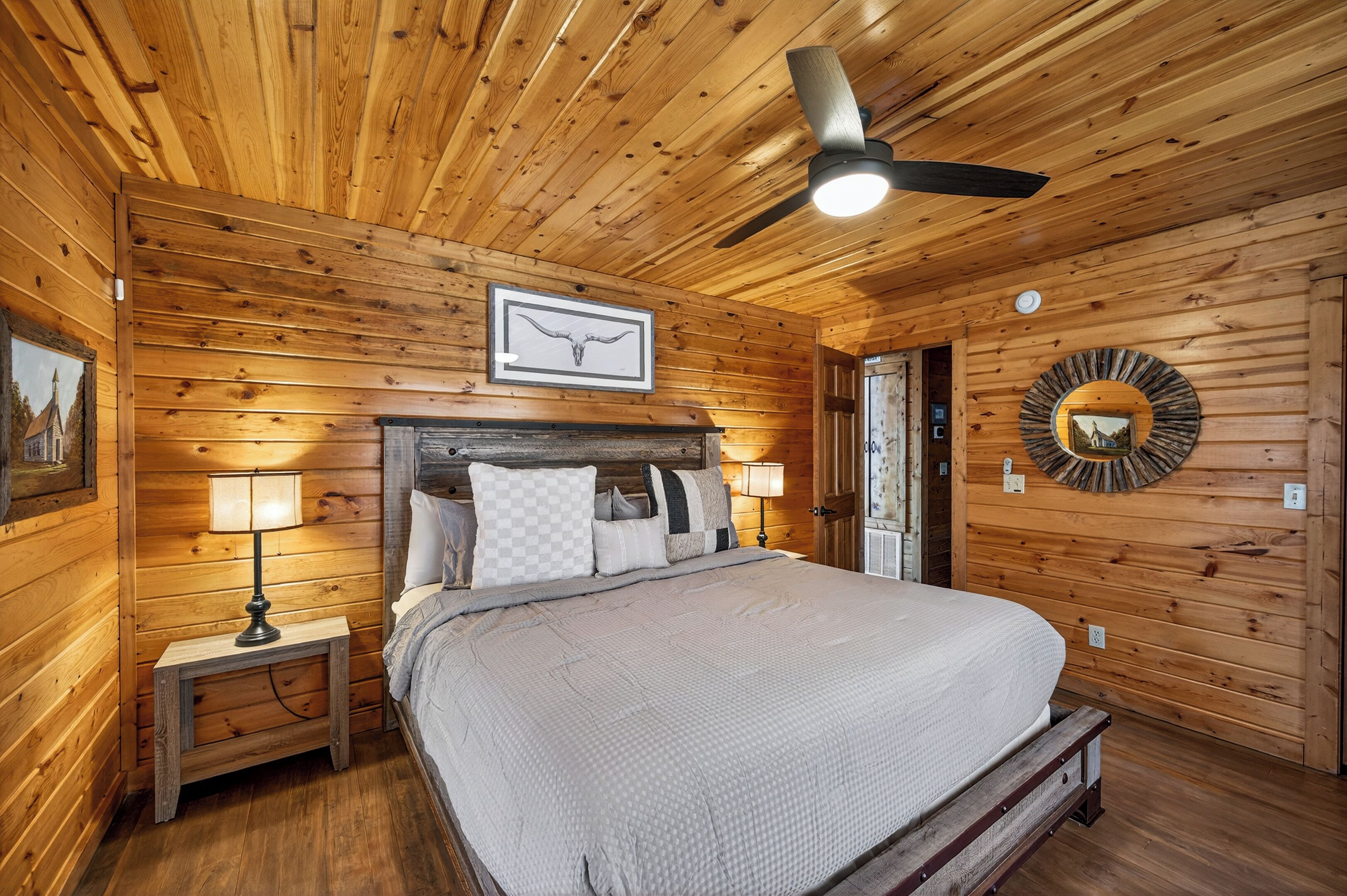 A wooden cabin bedroom with a bed, nightstands, a ceiling fan, and a wall-mounted mirror.