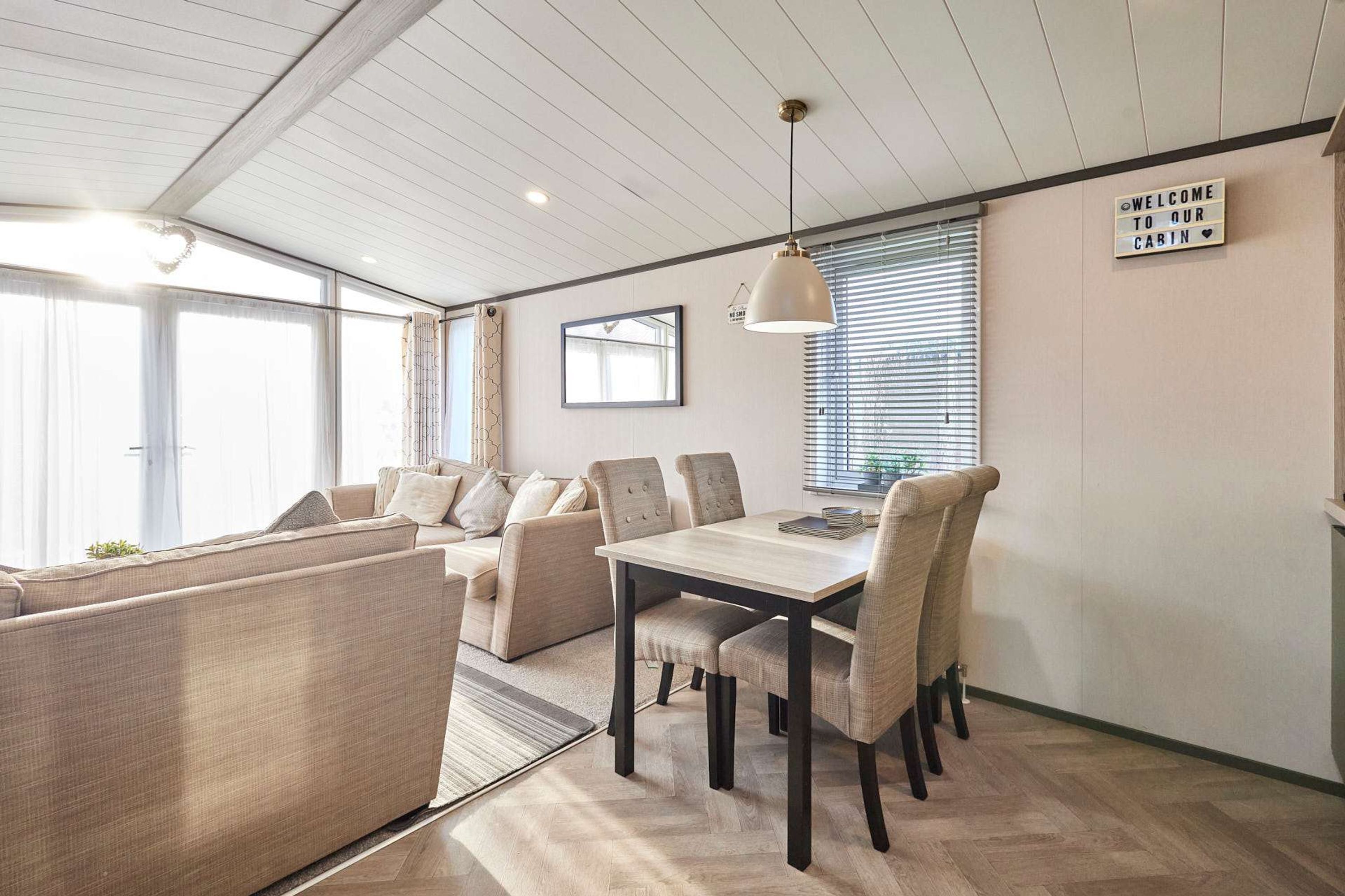 A modern cabin interior with a dining area, sofa, and a 'Welcome to our cabin' sign.