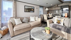 A modern living room with two sofas, a coffee table, and a kitchen area with a dining table. - Host Stay Coopers Cabin (Malton)