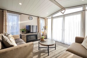 A modern living room with a sofa, coffee table, TV, and decorative items. - Host Stay Coopers Cabin (Malton)