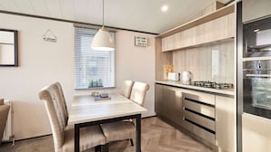 A modern kitchen with a dining area, featuring a wooden herringbone floor, a central island, and a built-in oven. - Host Stay Coopers Cabin (Malton)