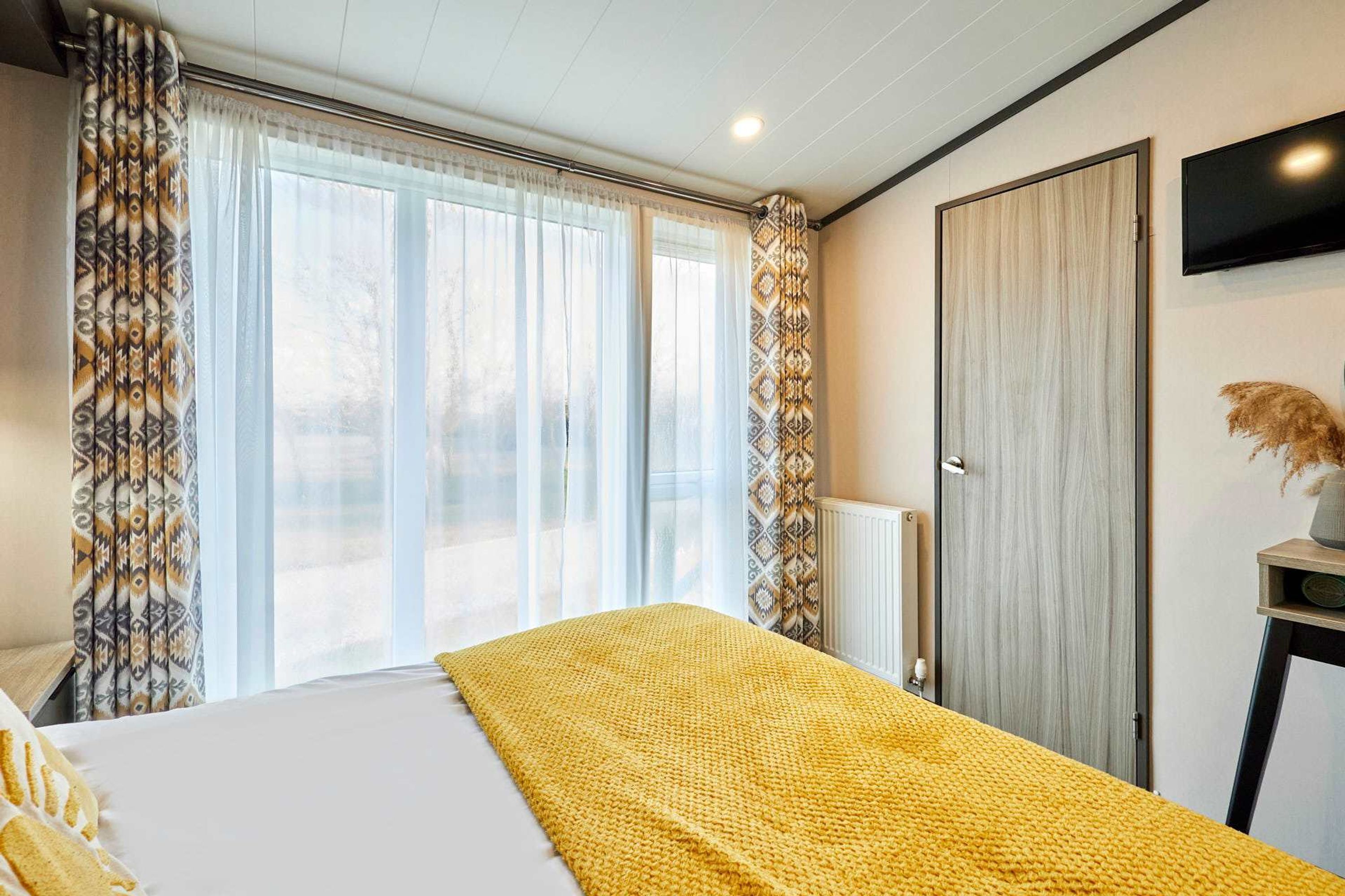 Habitación de hotel con cama, un ventanal con cortinas, un televisor en la pared y un radiador.
