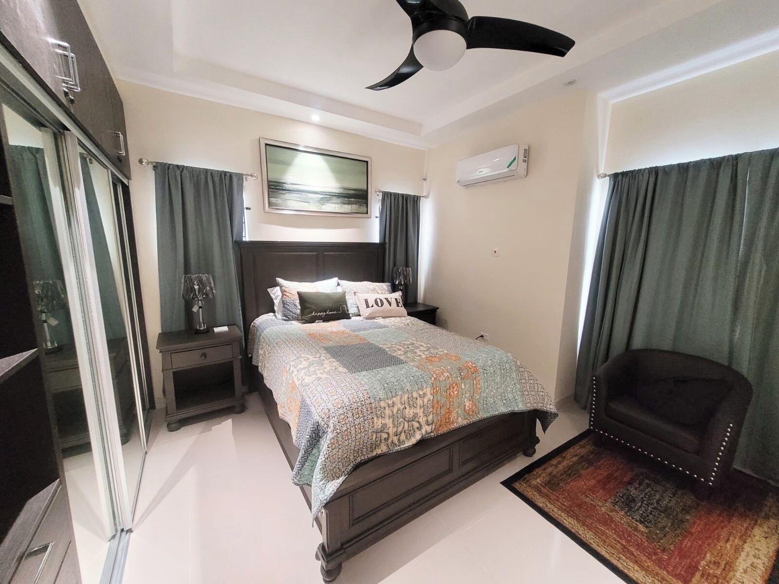 Une chambre à coucher comprenant un lit, une table de chevet, une chaise, un ventilateur de plafond et un appareil de climatisation.