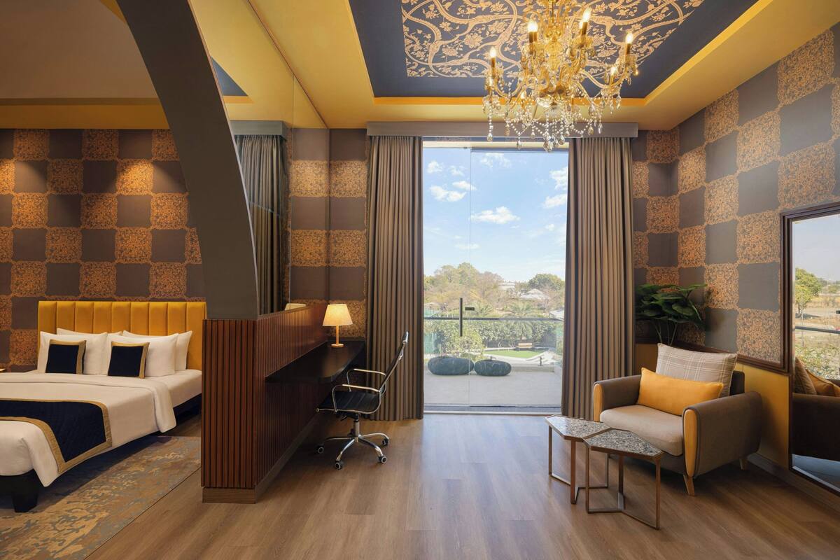 A hotel room with a large bed, a desk, a chair, a small table, and a view of the outdoors.