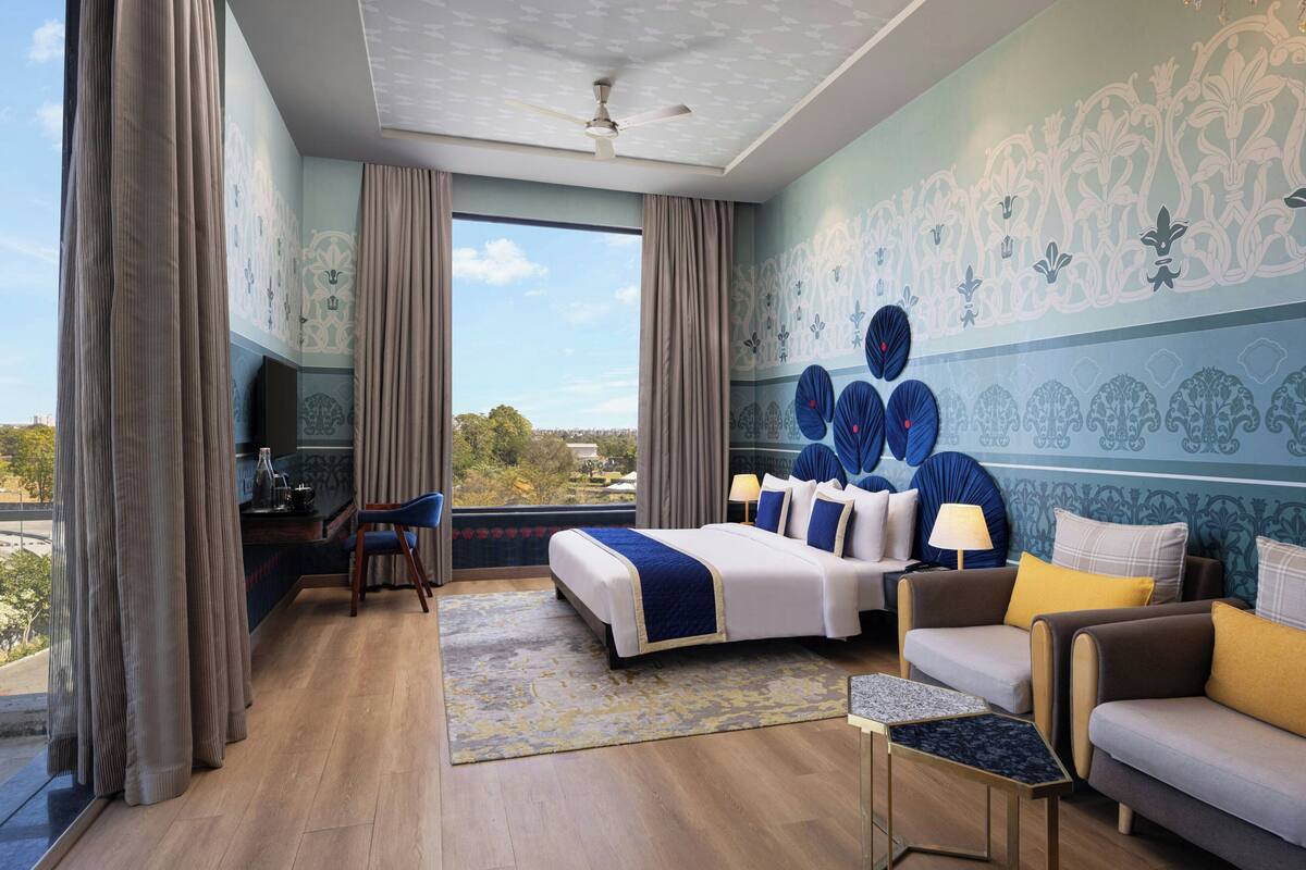 A hotel room with a bed, seating area, and a large window offering a view.