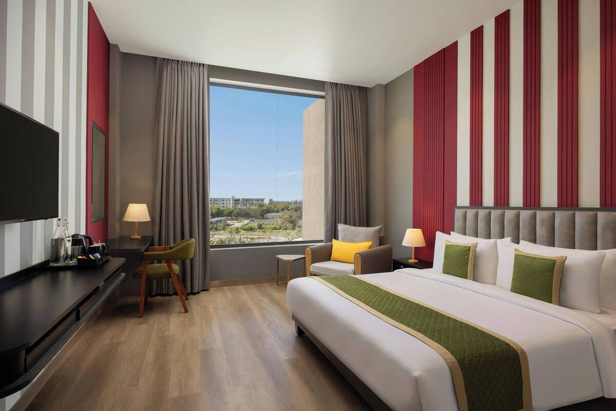 A hotel room with a bed, a desk, a chair, a TV, and a window with curtains.