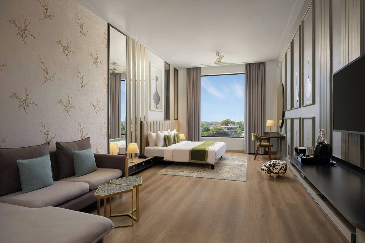 A hotel room with a sofa, a bed, a small table, a TV, and a view of the city.