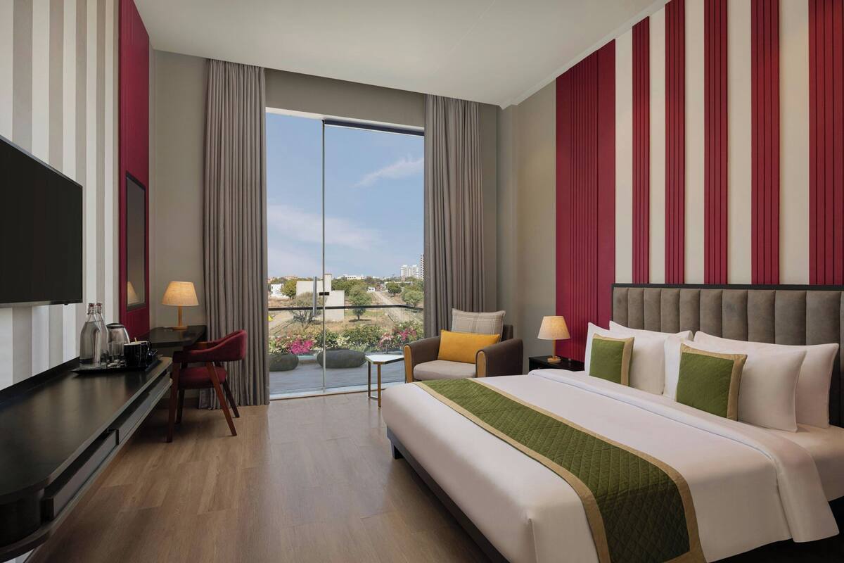 A hotel room with a bed, a desk, a chair, a TV, and a balcony with a view.