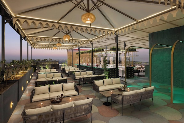 An outdoor seating area with wicker furniture, a covered section with a patterned ceiling, and a view of the cityscape.