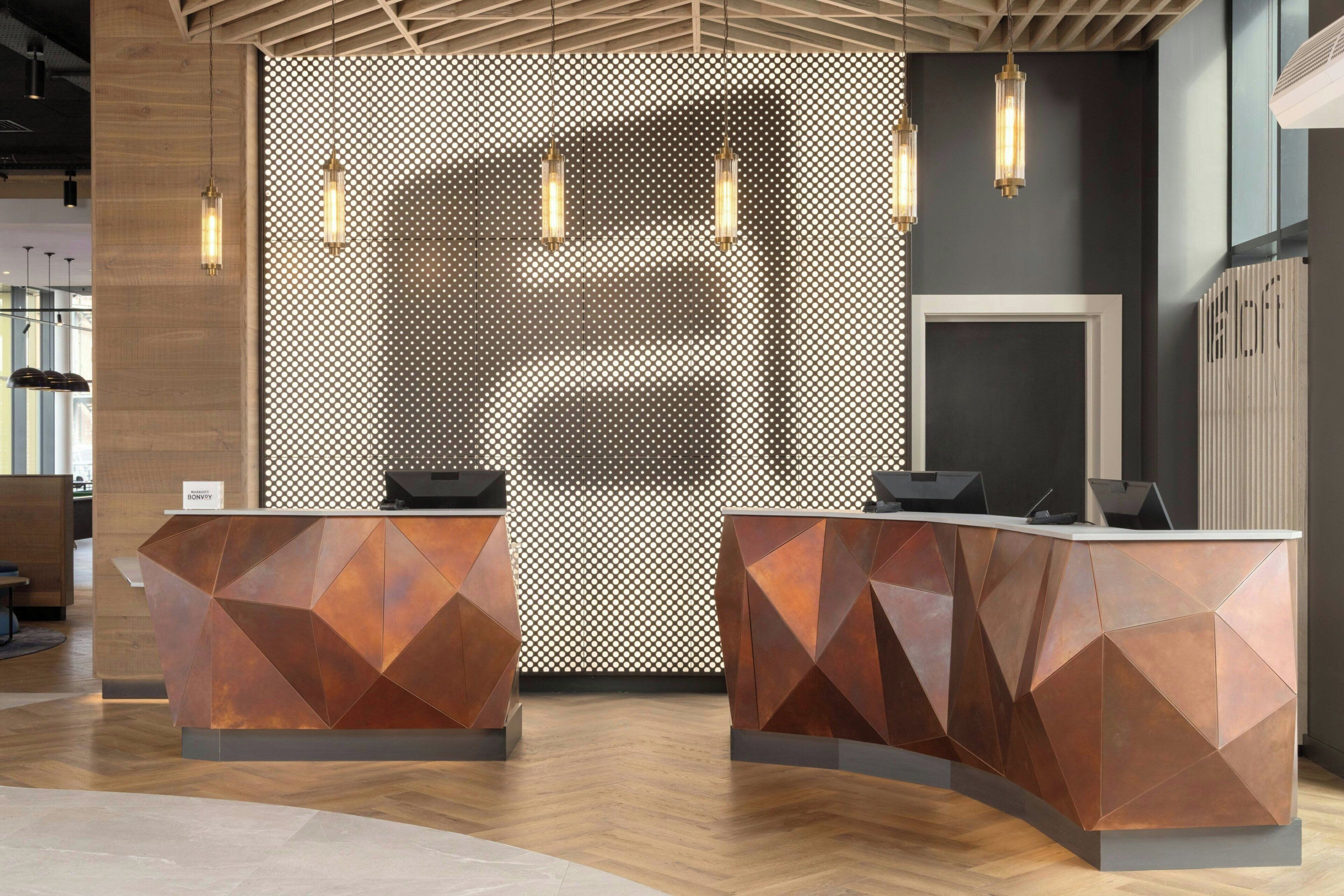 A reception area with geometric-patterned reception desks, a wooden ceiling, and hanging pendant lights.