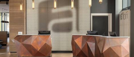 Zona de recepción con mostradores de diseño geométrico, techo de madera y lámparas colgantes.