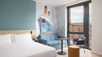 Una habitación de hotel moderna con una cama grande, un sofá azul, una mesita redonda y una silla.