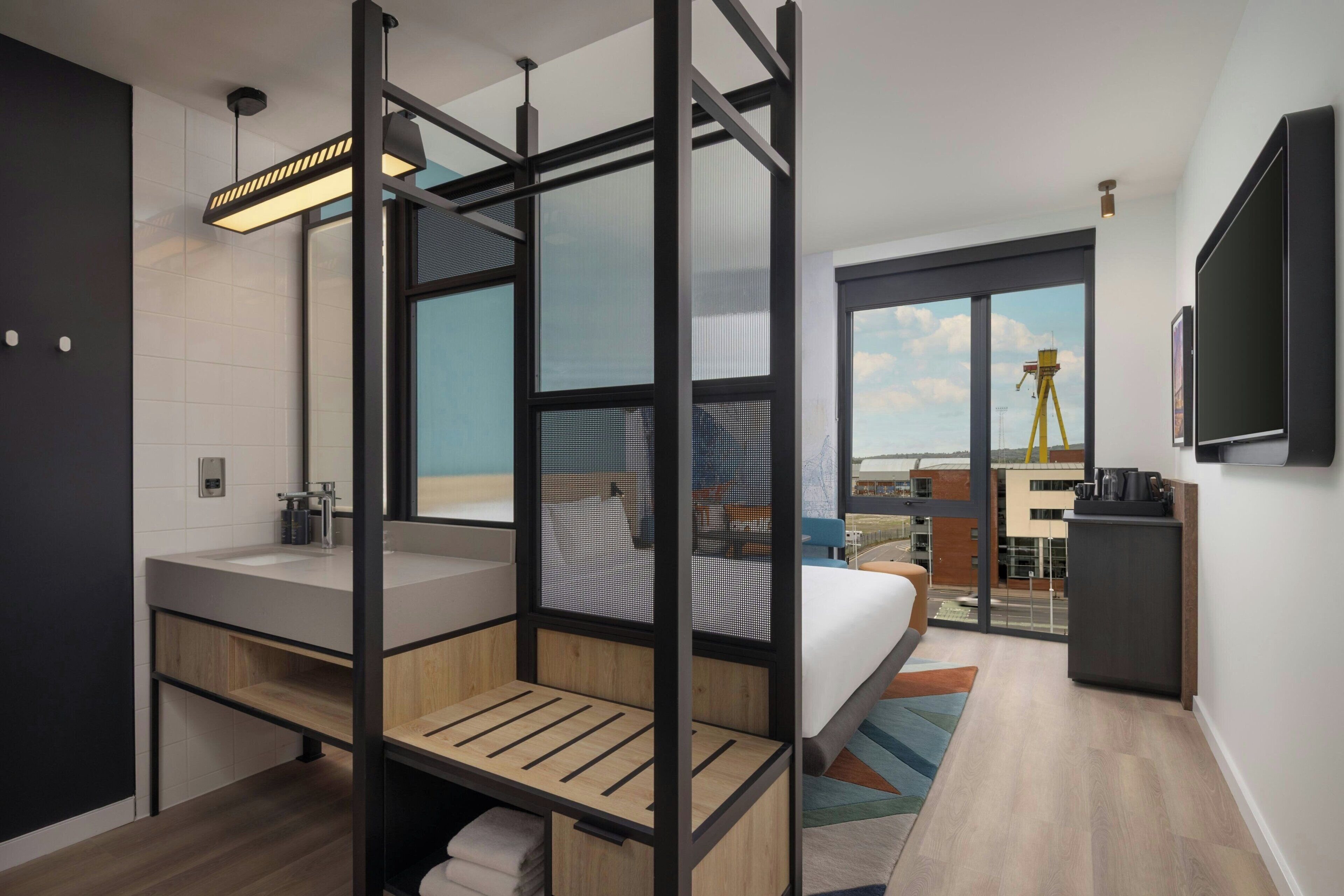 A modern hotel room with a large bed, a separate bathroom, a balcony with a view, and a mounted TV.