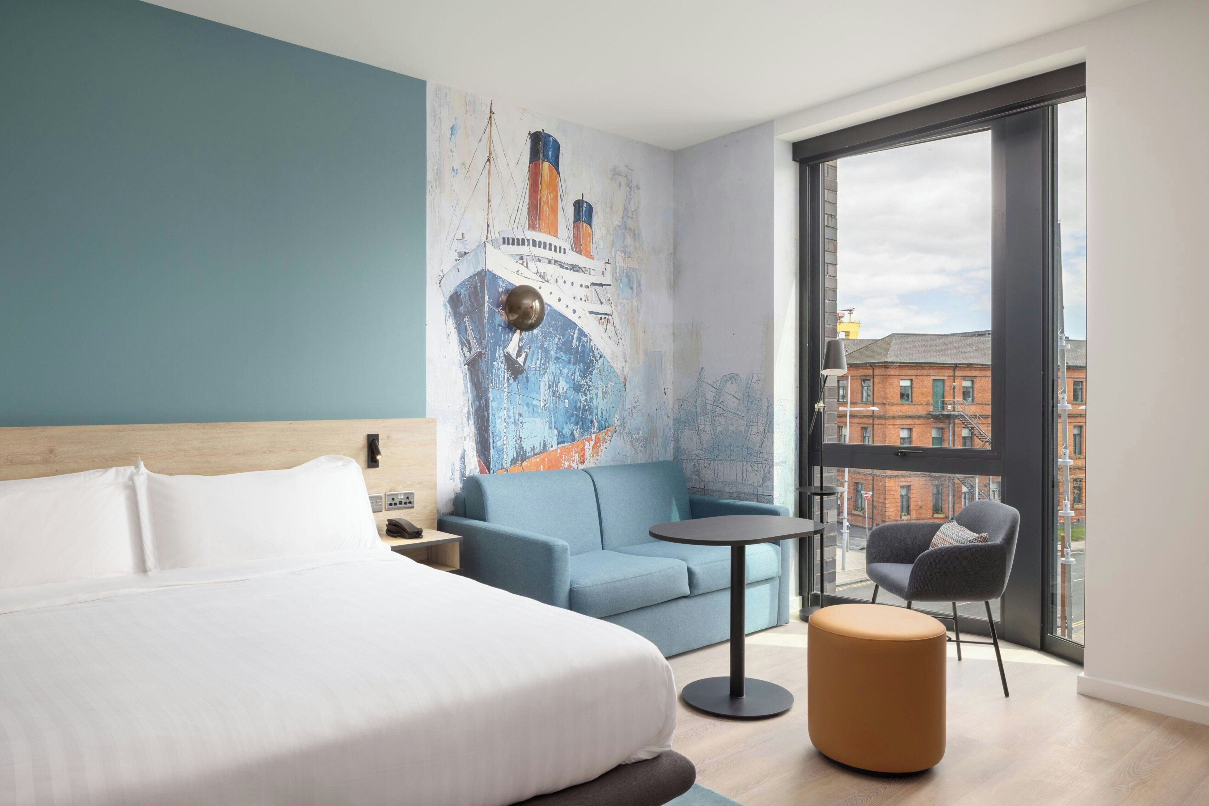 A hotel room with a bed, a blue sofa, a small round table, and a chair.