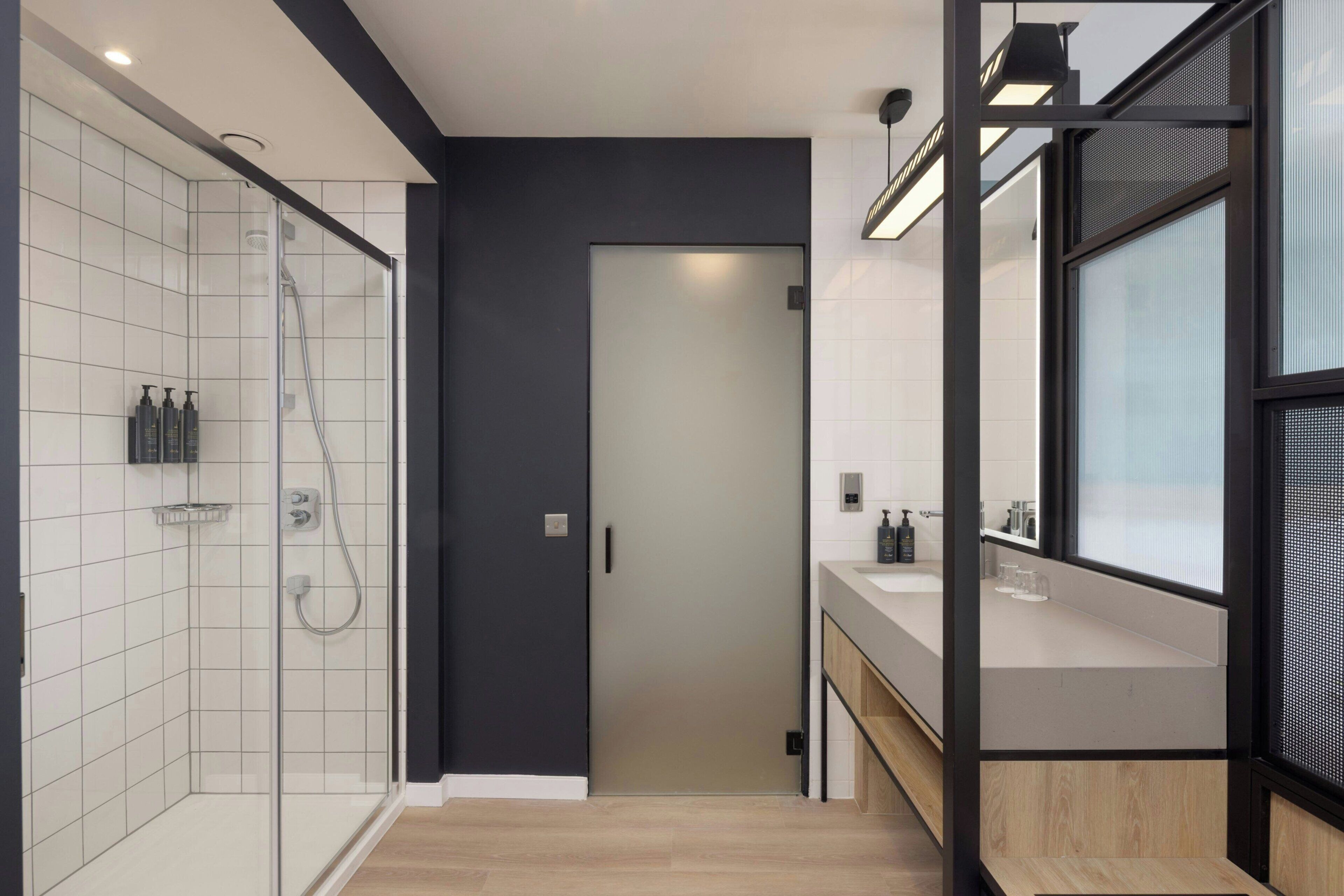 Un baño moderno con cabina de ducha de vidrio, una pared de acento oscura y un mueble de tocador de madera con espejo.