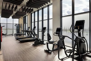 Un gimnasio con cintas de correr, elípticas y una máquina de remo, amplias ventanas y un techo alto.