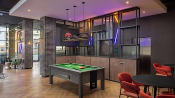 A pool table in a modern room with red chairs, a billiards rack, and a bar area with stools.