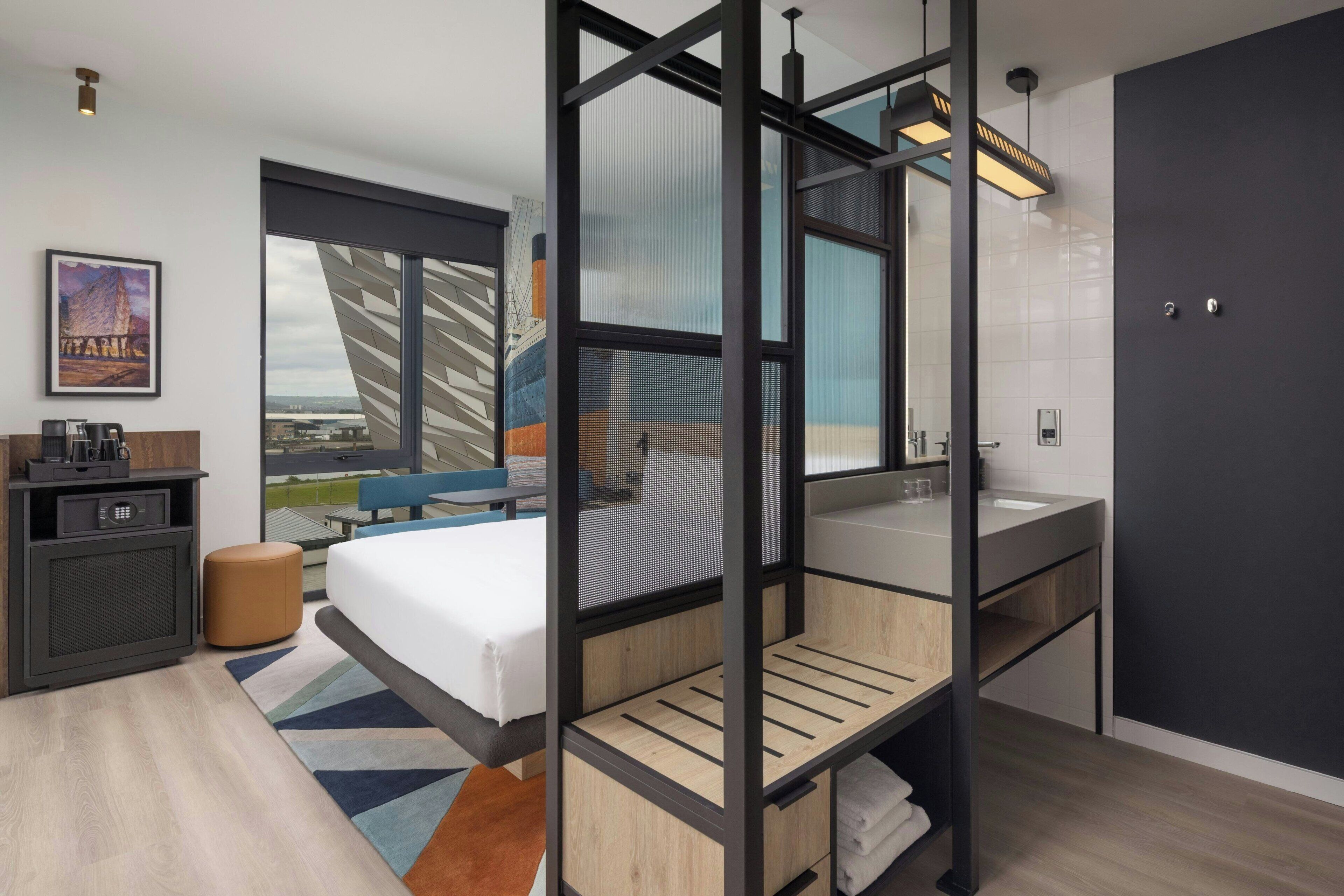 Une chambre d’hôtel moderne dotée d’un grand lit, d’un bureau, d’une salle de bain et offrant une vue sur le paysage urbain.