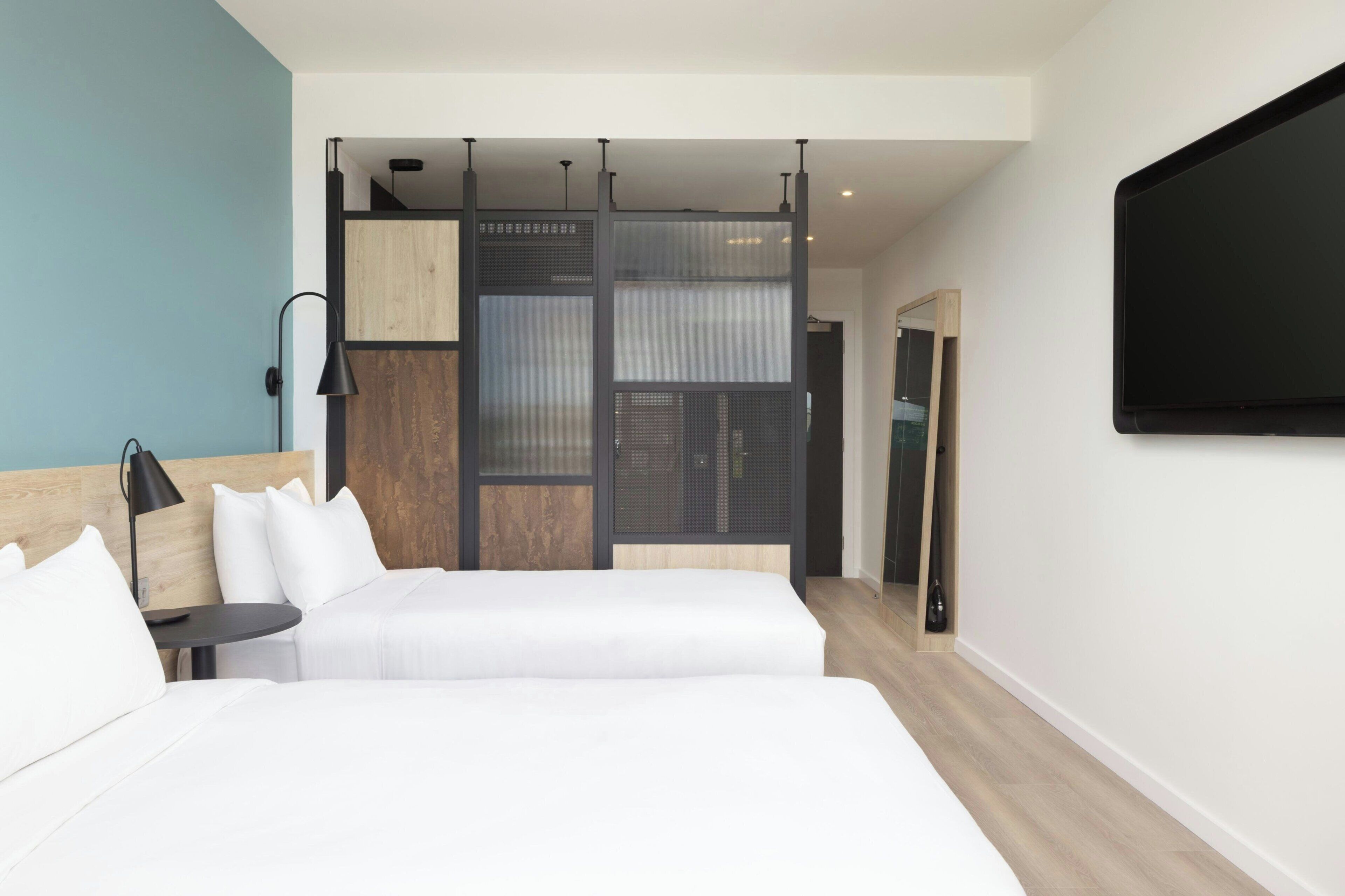 Una habitación de hotel moderna con dos camas, televisión y una puerta corredera.