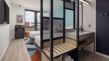 A modern hotel room with a bed, a desk, a large window, and a bathroom.