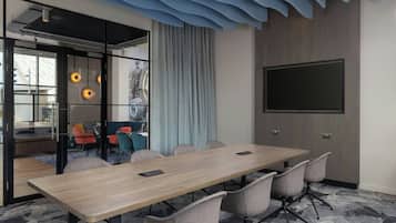 A conference room with a long table, six chairs, a large flat-screen TV, and a glass partition with a view.