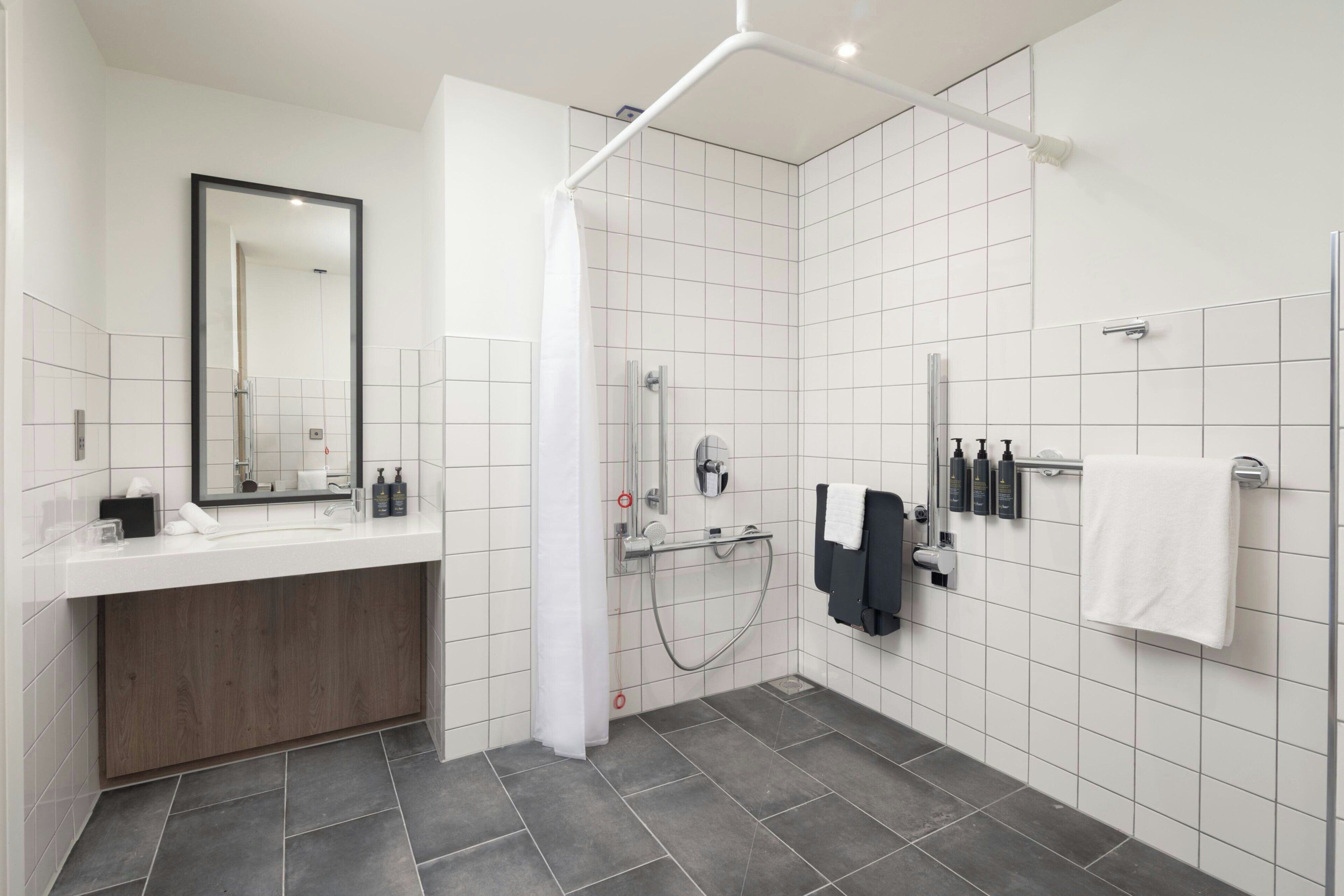 Ein modernes Badezimmer mit Dusche, Waschbecken, Spiegel und Handtuchhalter.