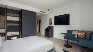 A modern hotel room with a bed, a sofa, a small table, a TV, and a desk with a computer.